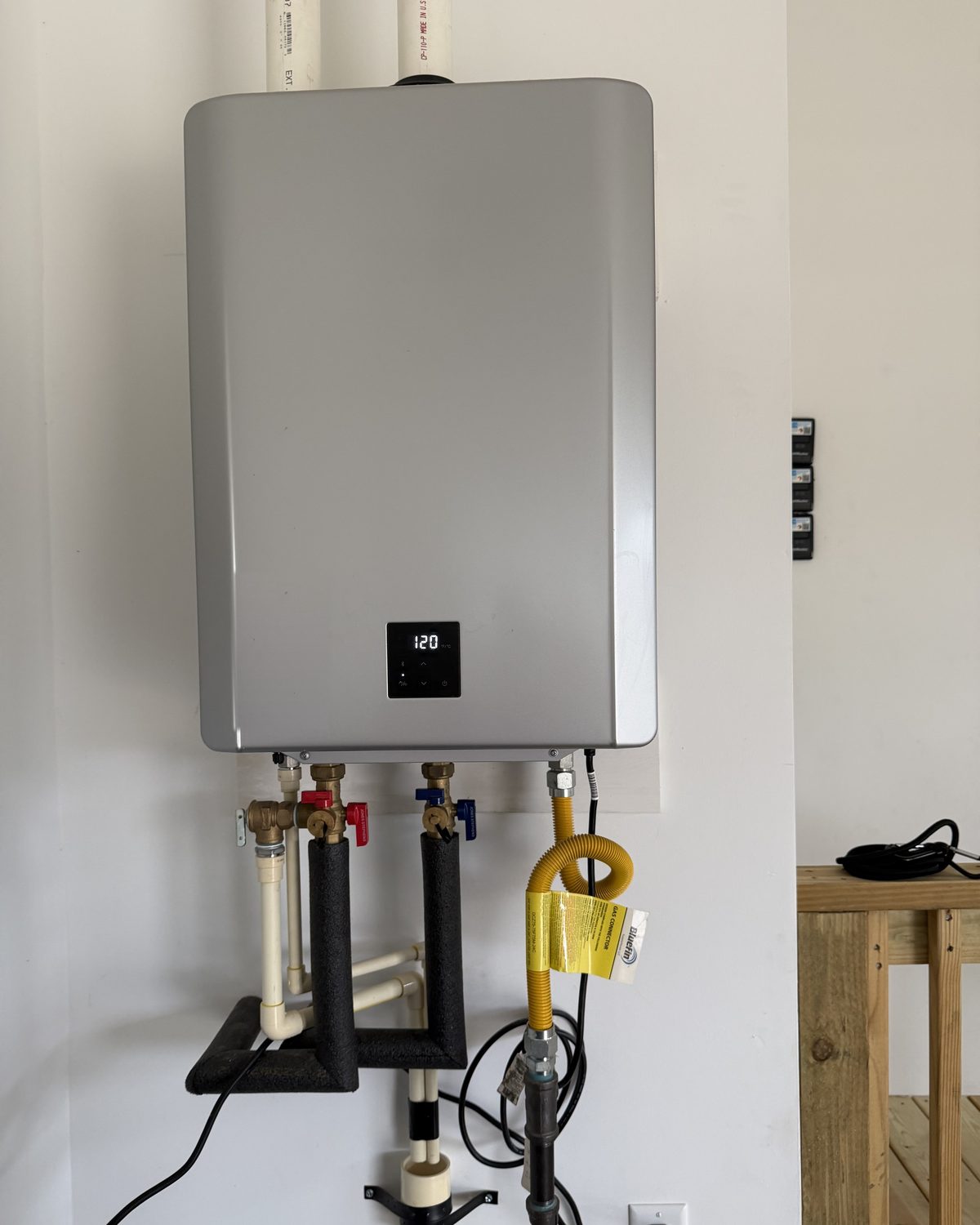 A condensing gas tankless water heater mounted on a white wall