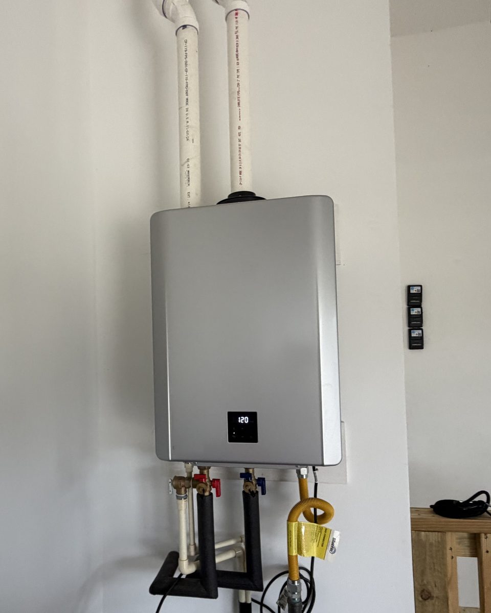 A condensing tankless water heater with two white plastic vent pipes running up from the top