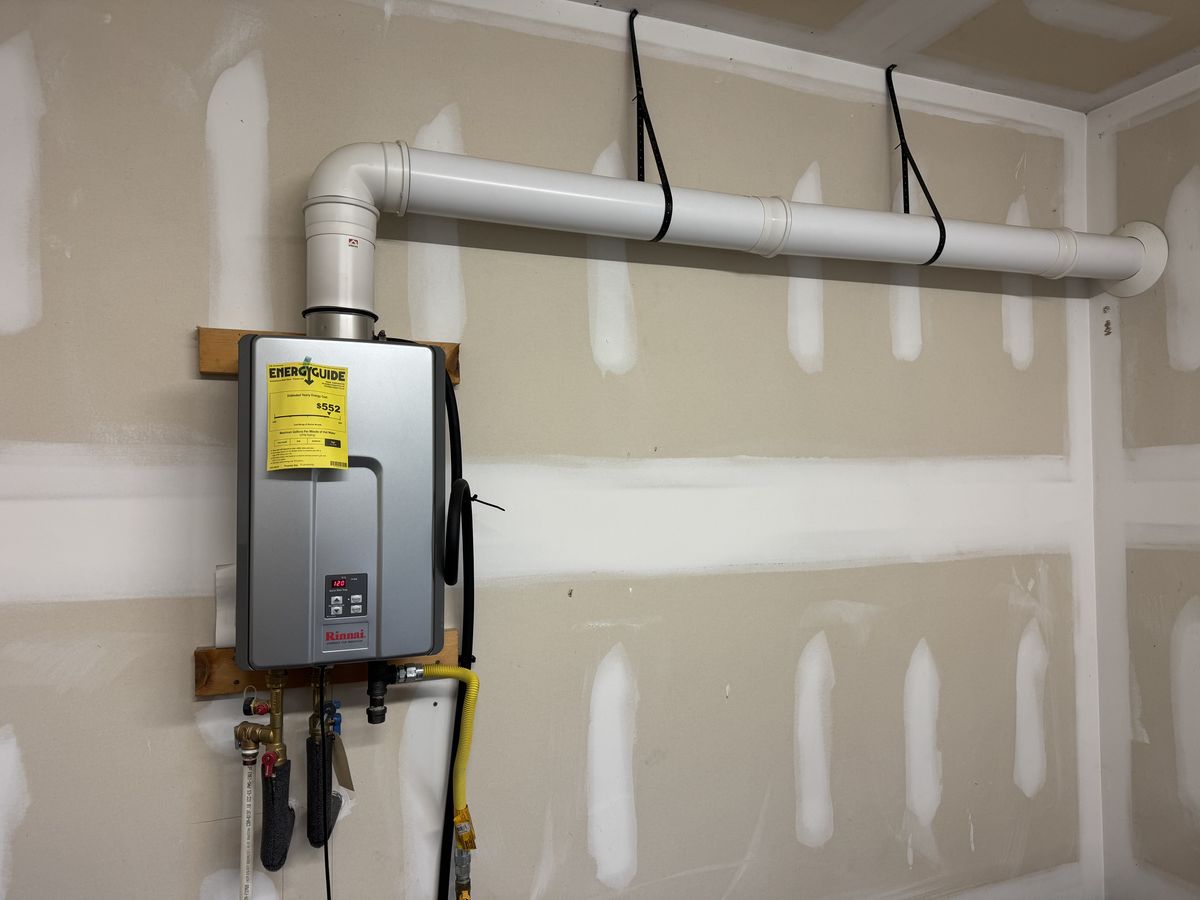 A tankless water heater in a garage with a long vent pipe running across the wall to the outside