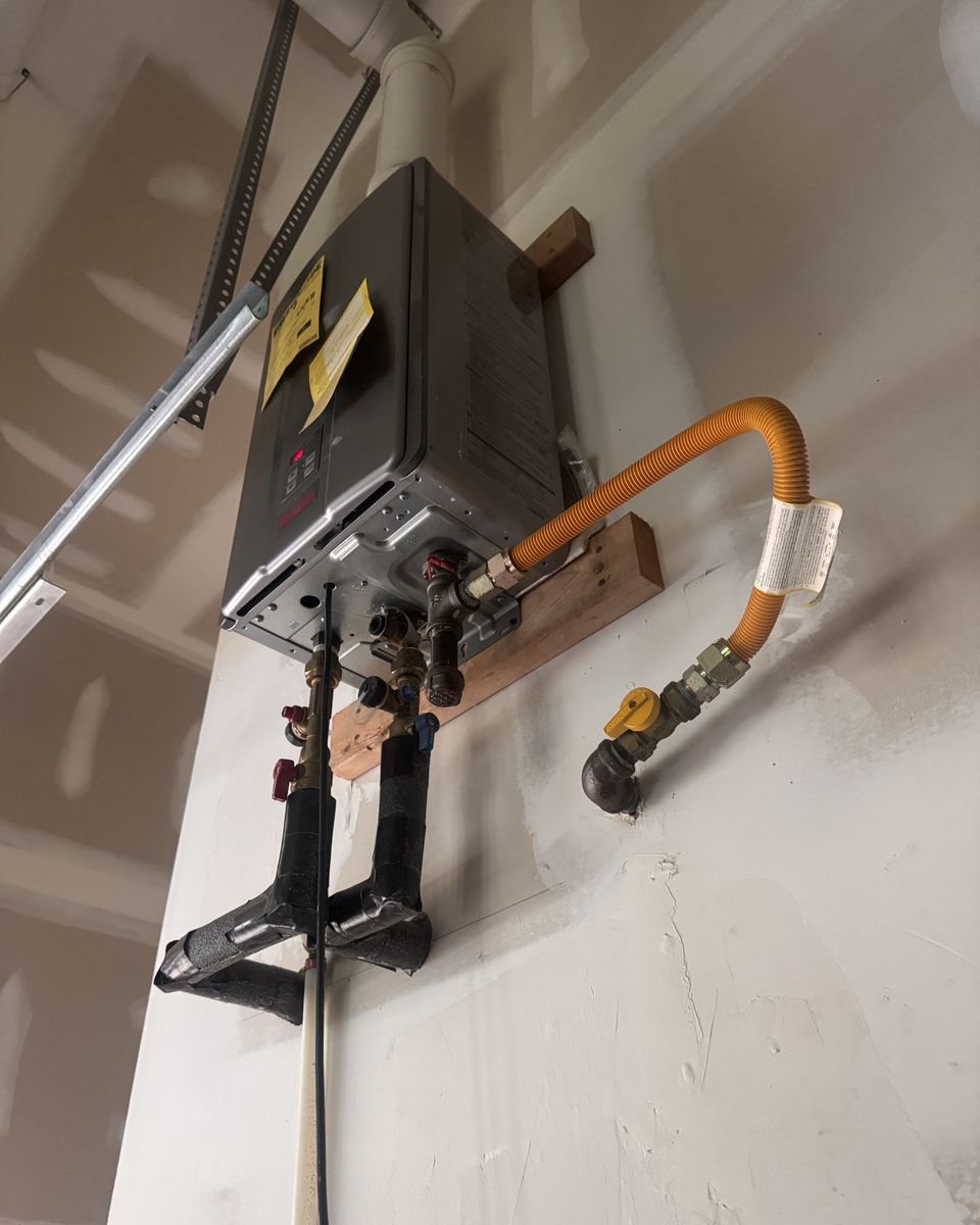 A tankless water heater mounted high on a garage wall with a flexible gas connector