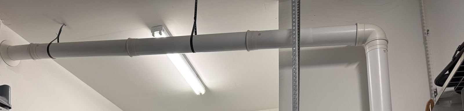 A vent pipe running across a garage ceiling from the water heater to an outside wall