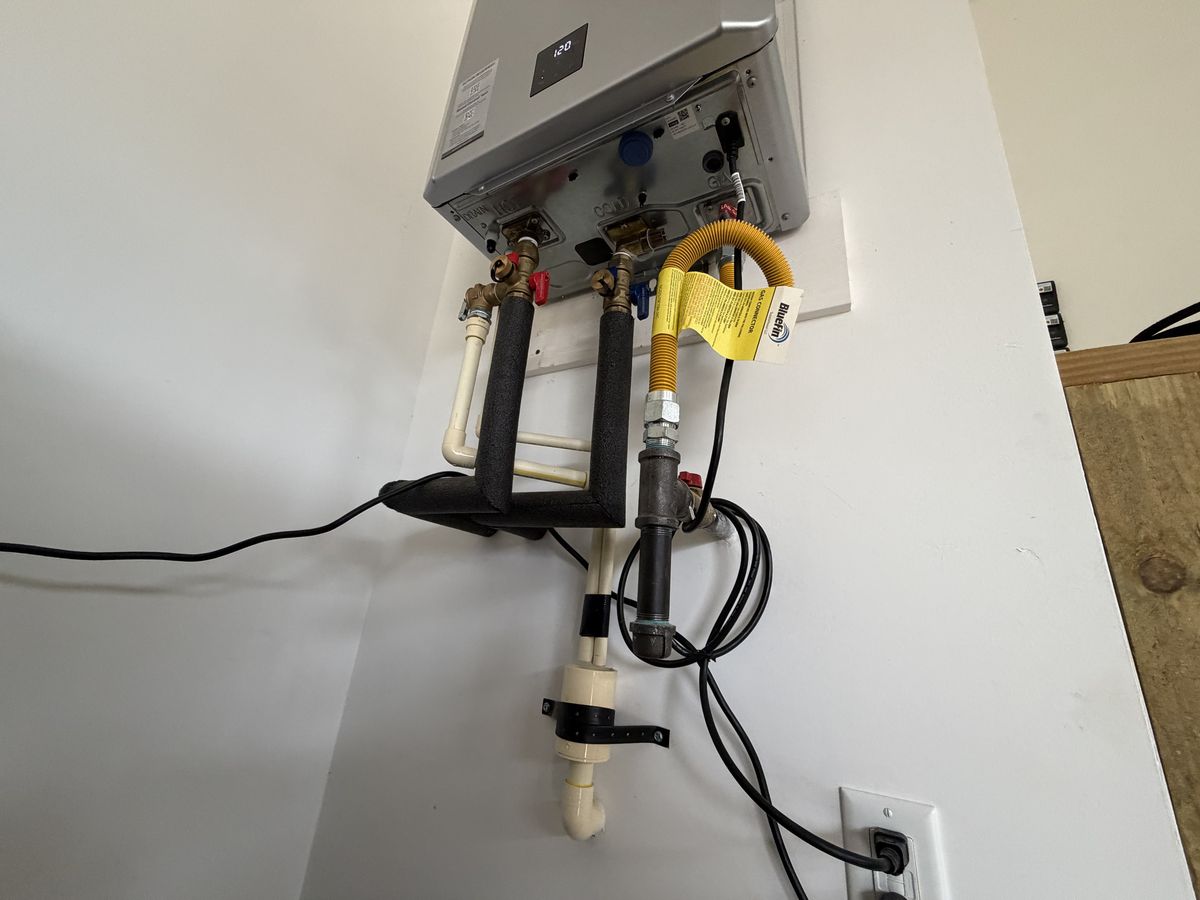 Close-up of insulated water lines, service valves, and a flexible gas connector under a tankless unit