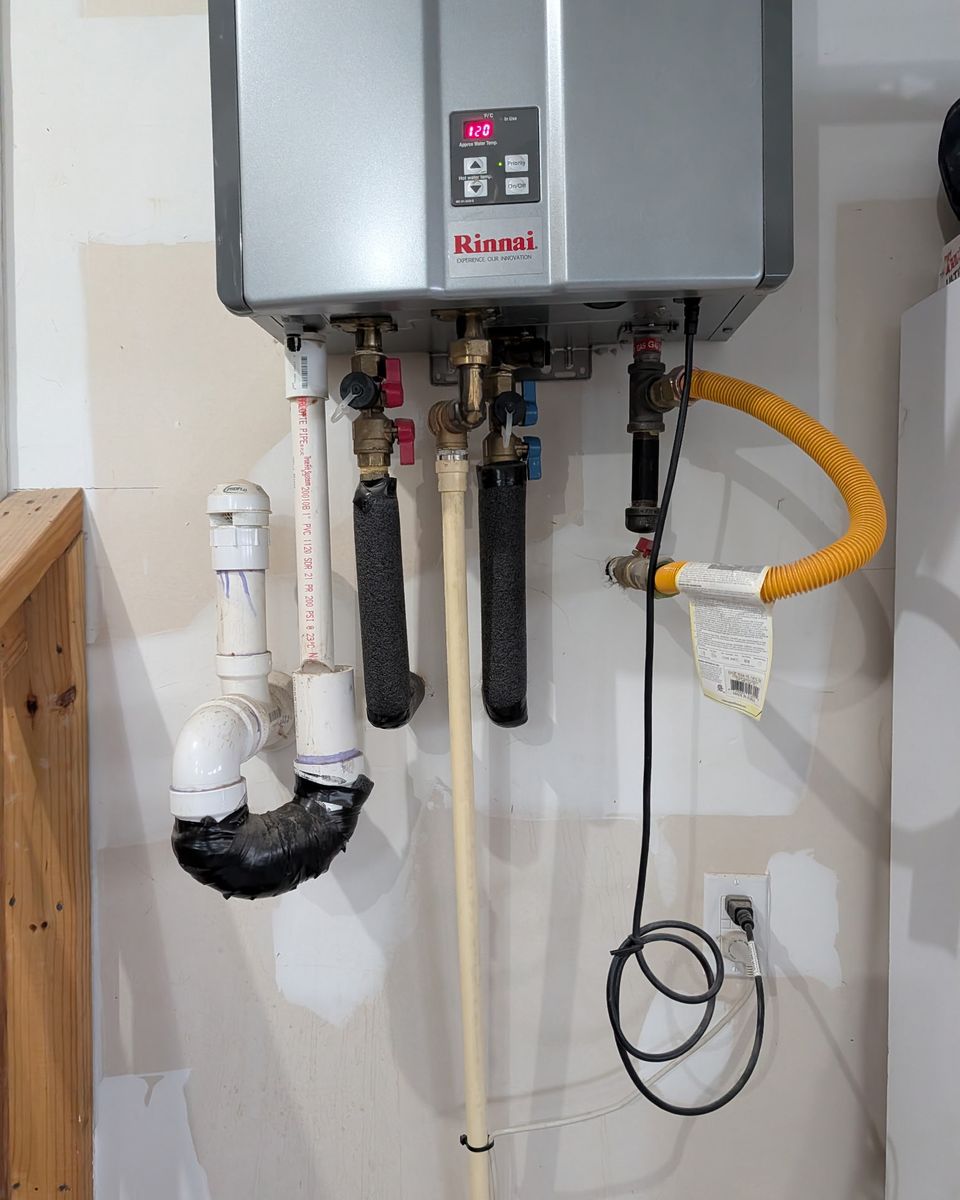 The water, gas, drain, and power connections under a condensing tankless unit