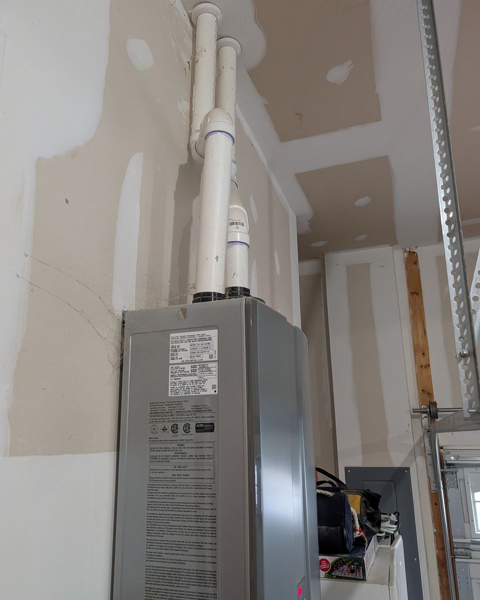 Two white plastic vent pipes rising from the top of a tankless unit through a garage ceiling