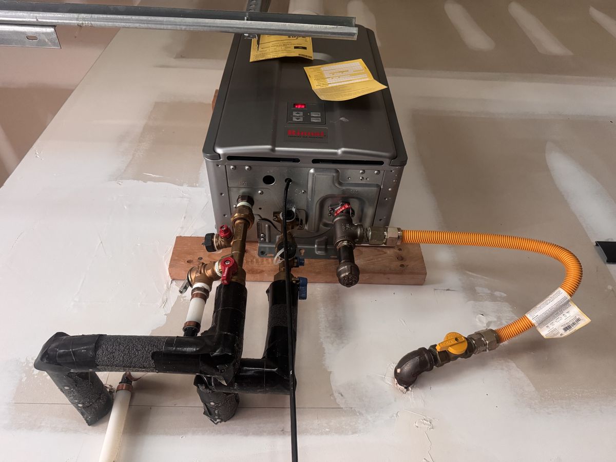 View from below of the water lines, service valves, and gas connection on a tankless unit