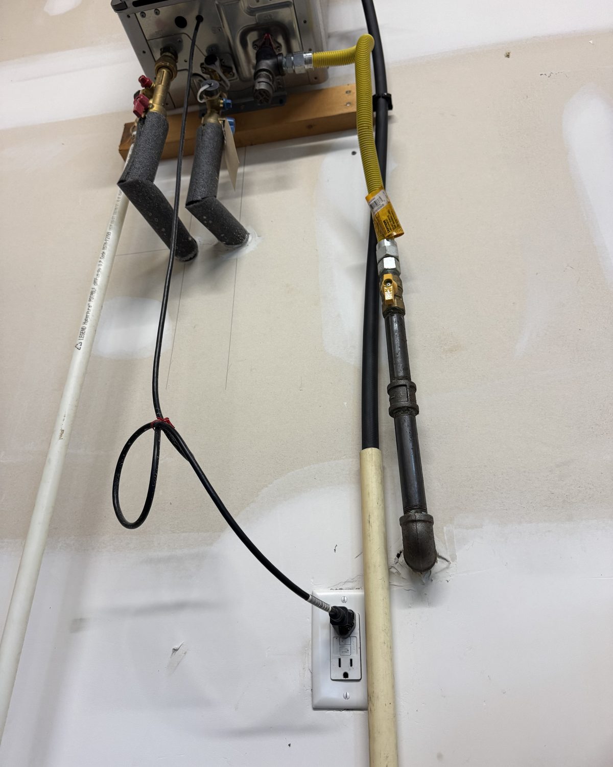 Water lines, a gas line with a yellow shutoff valve, and a power cord below a tankless unit